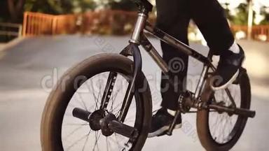 无法辨认的极端bmx自行车骑在他的黑色自行车在一个阳光明媚的溜冰公园夏天。 酷年轻的宝马自行车